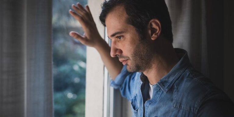 Pensive man looking out winder thinking about methadone vs suboxone treatment programs