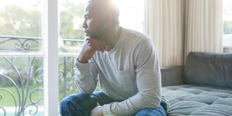 Concerned man looking out window thinking about opioid agonists and antagonists for addiction treatment