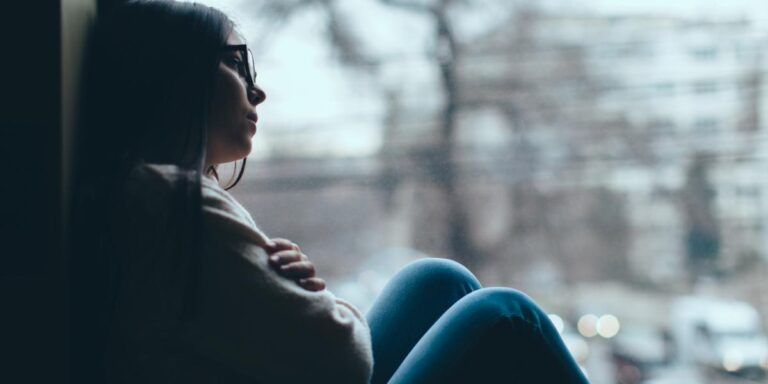 Woman sitting in the dark near a window thinking about subutex vs suboxone treatment