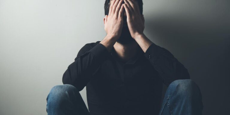 Man sitting against wall covering his face with his hands wondering if naloxone will cause withdrawal