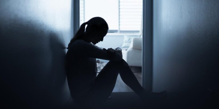 person sitting on floor in hallway struggling with the long term effects of drug addiction